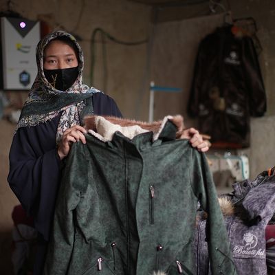 Zainab, a tailor in Afghanistan, proudly holds up a finished coat she made.
