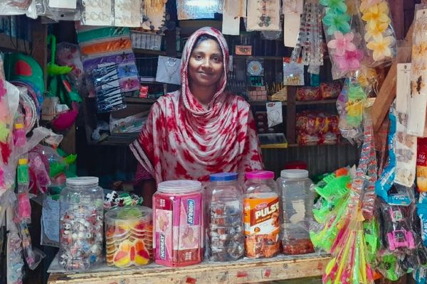 A woman wearing red and white stands amid her goods at her shop and smiles