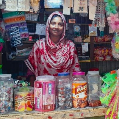 A woman wearing red and white stands amid her goods at her shop and smiles