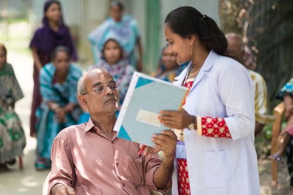 A BRAC health worker supports a man to get new reading glasses in Bangladesh.