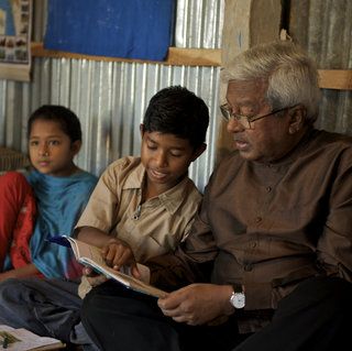 Sir Fazle Hasan Abed sits with three children as one points to the book he holds.