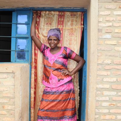 A woman in a pink and purple outfit stands in her blue doorway and smiles at the camera with pride