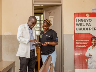 A man in a white lab coat and a woman in a black top look at a tablet running a digital mHealth solution designed to enhance service quality