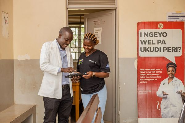 A man in a white lab coat and a woman in a black top look at a tablet running a digital mHealth solution designed to enhance service quality