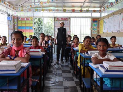 A Rohingya teacher stands at the back of a classroom of female students
