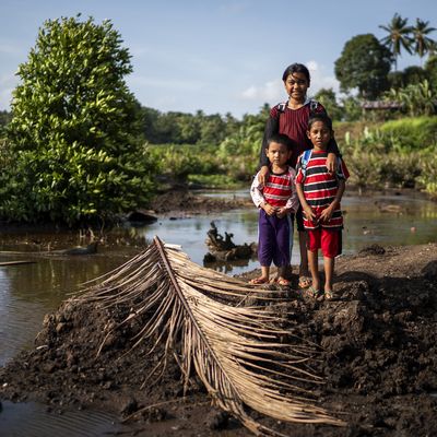 A girl and two younger boys stood by water on a mud bank