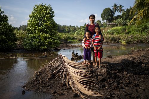 A girl and two younger boys stood by water on a mud bank
