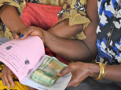 A woman holds a booklet and a small collection of cash during a meeting