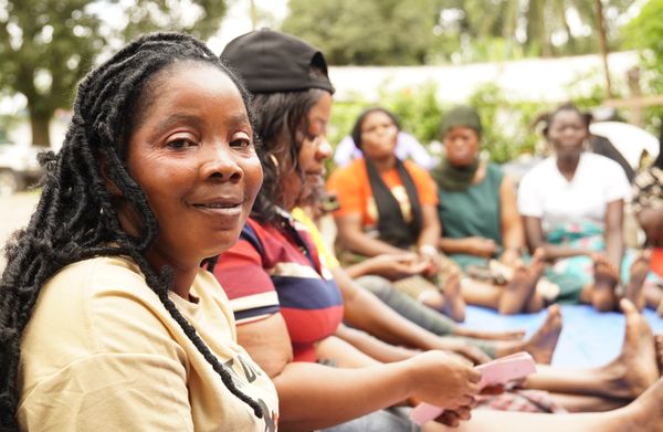 A group of Liberian BRAC MF clients sit in discussion and one of them looks at the camera