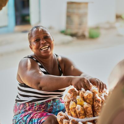A Ghanian woman smiles as she rests her hands on top of a neatly stacked display of produce