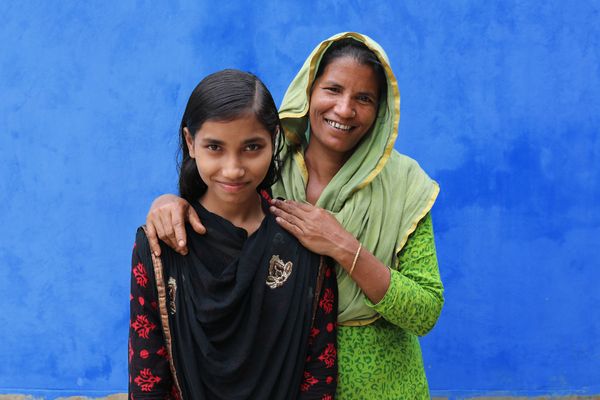 A mother and daughter in Bangladesh in front of blue wall.