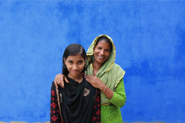 A mother and daughter in Bangladesh in front of blue wall.
