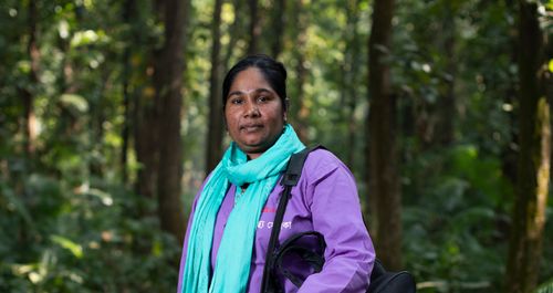 Nilafur Yasmin poses on a forest path in her community health worker uniform.