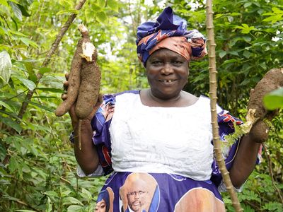 BRAC Microfinance Liberia MF client holds up produce while working in her field with a smiling face