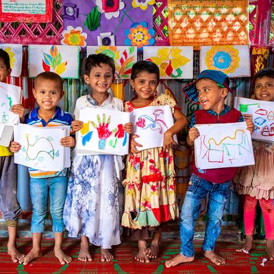 Rohingya refugee children smile with their artwork at a Humanitarian Play Lab in Cox's Bazar, Bangladesh