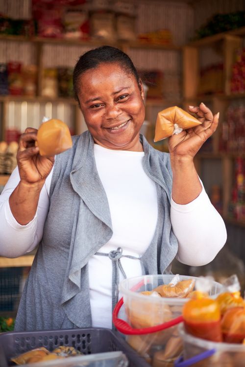 A Ghanian woman smiles at the camera while showing food items for sale