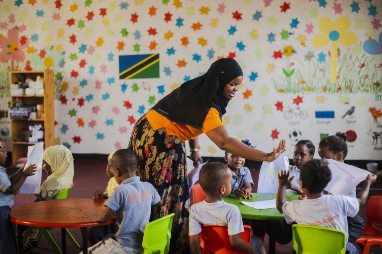 A Play Leader (teacher) talks to a group of young children in a colorfully decorated BRAC Play Lab.