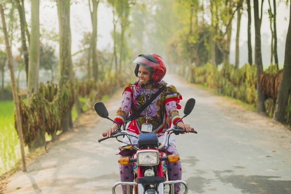 A female BRAC staff member rides a motorcycle to work