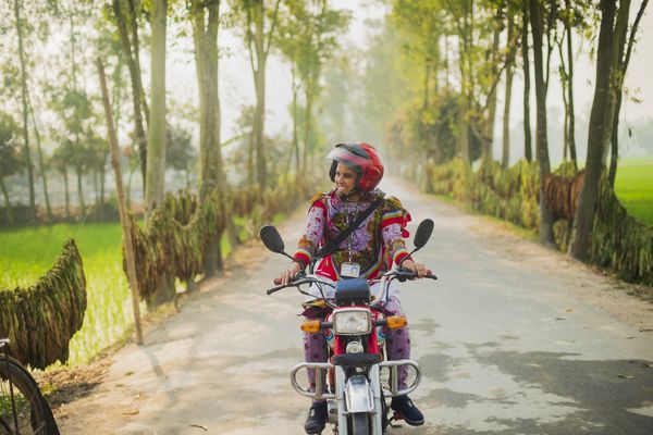 A female BRAC staff member rides a motorcycle to work