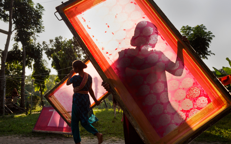 Two women holding screens face away from the camera while outside. They are artisans behind Bangladesh's leading lifestyle brand, Aarong
