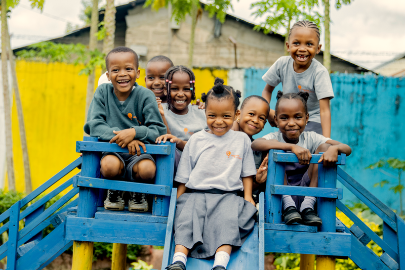 A group of happy young children are playing on a blue wooden structure outdoors.