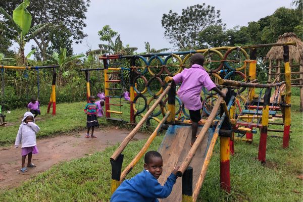 Children play on a play structure outside made of tires and wood.