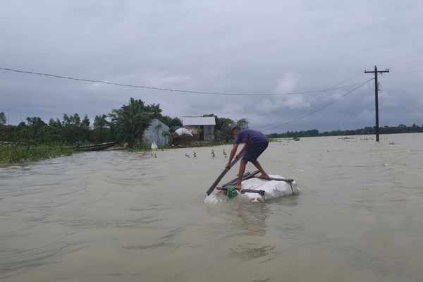 Under gray skies, a man leans forward on a makeshift raft to navigate flooding