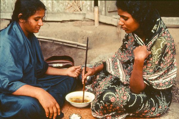 An Oral Rehydration Worker in her blue saree uniform checking whether a rural mother remembers the recipe and can recreate the recipe on her own as part of the project's monitoring system