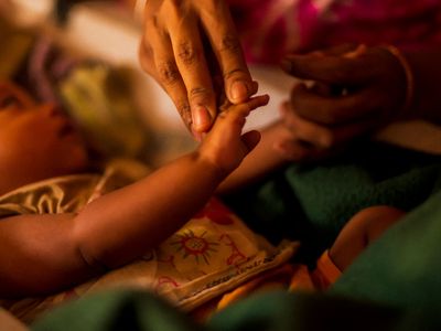 A young baby's hand is held gently by an adult.