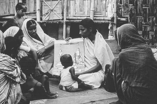 A monochrome photo of an Oral Rehydration Worker in her blue saree uniform teaching rural mothers sitting in a circle the causes of diarrhoea and how the disease causes deadly dehydration in children in the early days of the Oral Rehydration Therapy