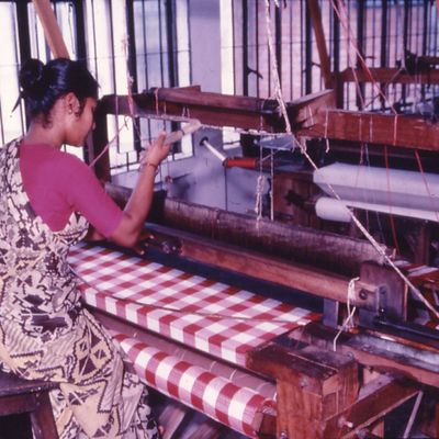 An artisan sits at her loom to create a red and white checkered fabric