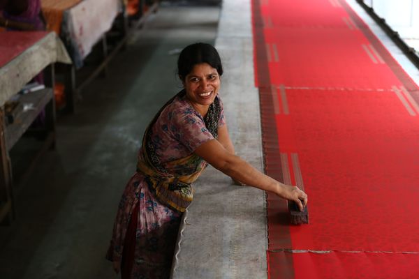 A female artisan looks at the camera while working on a red piece of fabric