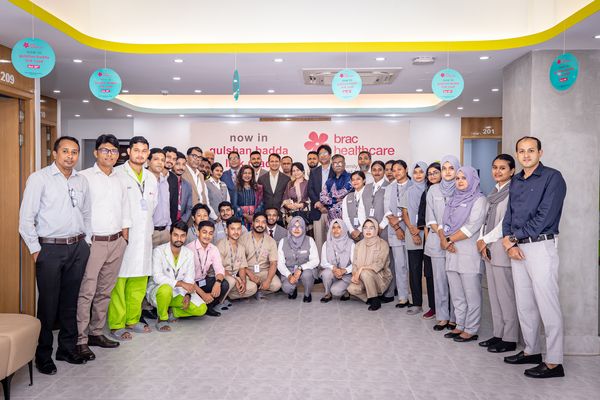 A group of about 40 BRAC Healthcare employees smile as they celebrate the opening of a new Healthcare office