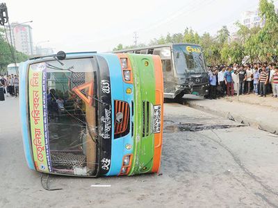 A bus fallen on its side in the middle of the street with lots of pedestrians walking by