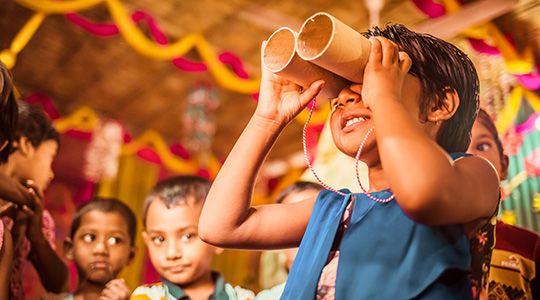 A child attempts to watch through paper made binoculars smiling