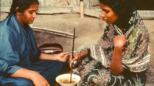 Two women sit down eating a soup.