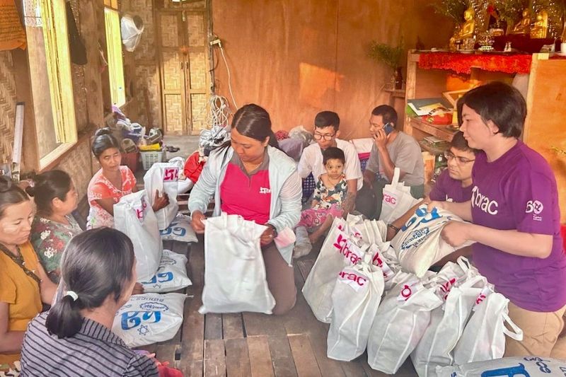 A woman sits amid a circle of women. She wears a pink BRAC shirt and has a bag of emergency aid items in front of her.