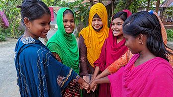 Five girls stand in a semi-circle holding hands.
