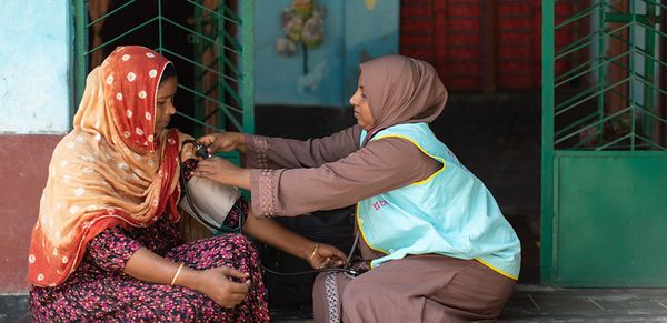 A community health worker takes a woman's blood pressure on a doorstep in Bangladesh.