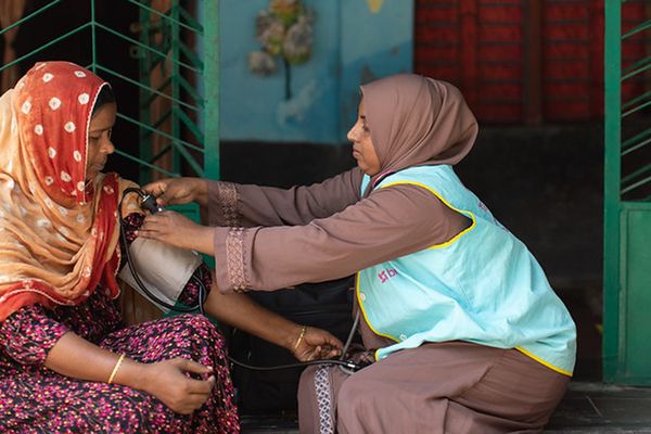 A community health worker takes a woman's blood pressure on a doorstep in Bangladesh.