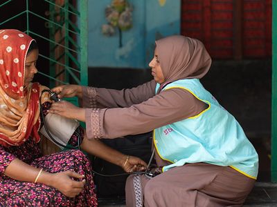 A community health worker takes a woman's blood pressure on a doorstep in Bangladesh.