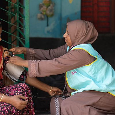 A community health worker takes a woman's blood pressure on a doorstep in Bangladesh.