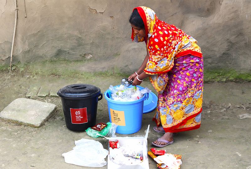 নিজ বাড়িতে দুটি আলাদা বিনে জৈব ও অজৈব বর্জ্য আলাদা করছে একজন গ্রামীণ নারী