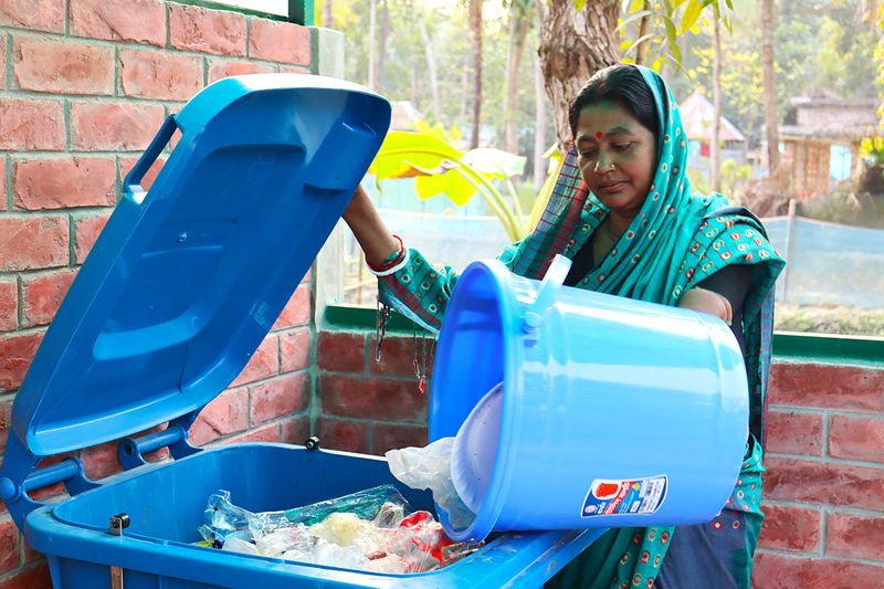 কেন্দ্রীয় বর্জ্য ব্যবস্থাপনা শেডে নির্দিষ্ট বিনে প্লাস্টিক বর্জ্য ফেলছেন একজন গ্রামীণ নারী