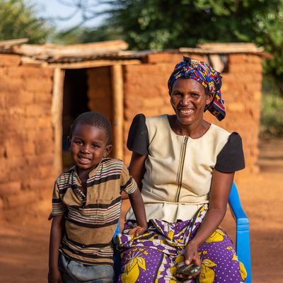 UPGI participant in Kenya holding a phone and smiling at the camera along with her smiling child